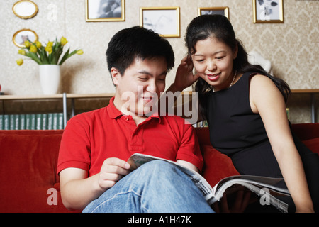 Jeune couple assis sur un canapé la lecture d'un magazine Banque D'Images