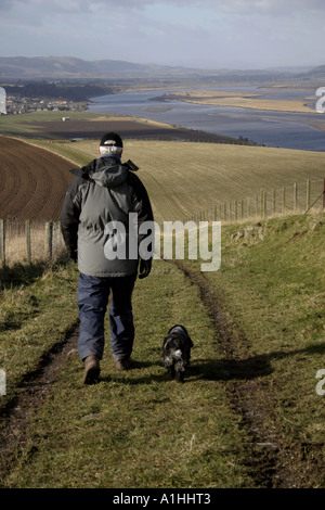 Homme marchant avec son chien dans la région de Fife en Écosse avec rivière Tay en arrière-plan Banque D'Images