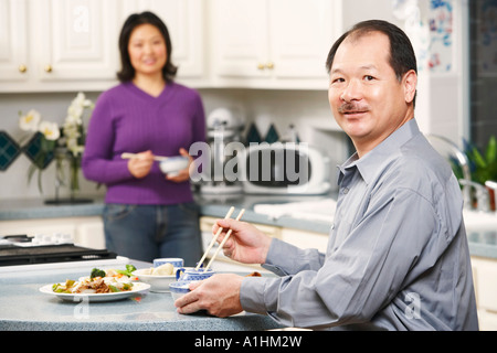 Portrait of a senior man holding a paire de baguettes avec une femme mature se tenant derrière lui Banque D'Images