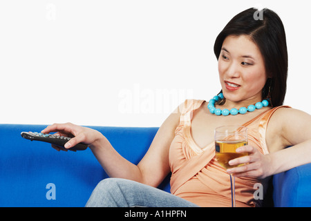 Portrait d'une jeune femme tenant un verre de vin et d'une télécommande Banque D'Images