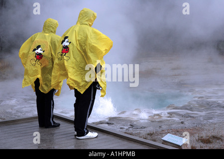 Deux personnes en capes de pluie jaune sur la demande à la recherche au près de Old Faithful Geyser spasmodique dans le Parc National de Yellowstone Banque D'Images