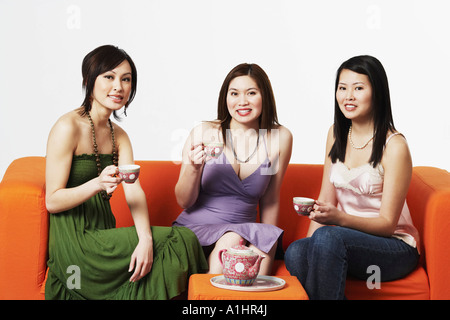 Portrait de trois jeunes femmes assises sur un canapé avec verres Banque D'Images