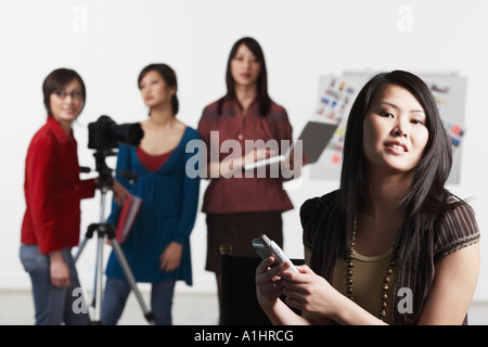 Portrait of a young woman holding a mobile phone avec ses amis debout derrière elle Banque D'Images