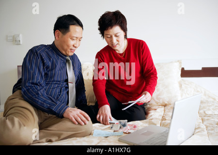 High angle view of a young couple assis sur le lit avec du papier-monnaie et d'un ordinateur portable