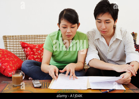 Jeune couple assis sur un canapé et la lecture de documents Banque D'Images