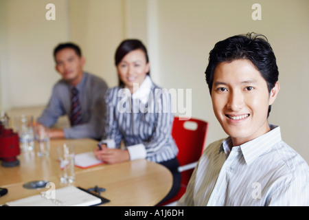 Portrait d'un homme assis à une table de conférence et souriant avec deux collègues Banque D'Images