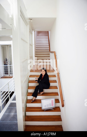 Portrait d'une femme assise sur un escalier et holding a mobile phone Banque D'Images