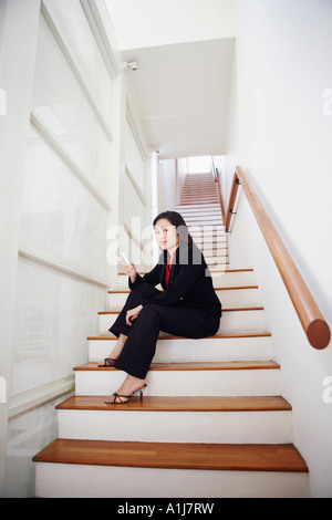 Portrait d'une femme assise sur un escalier et à l'exploitation d'un téléphone mobile Banque D'Images
