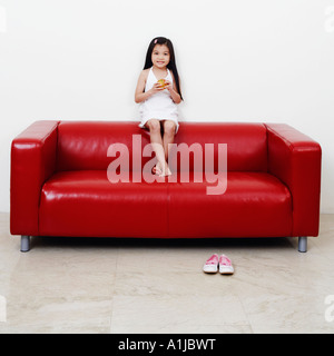 Portrait d'une fille assise sur un canapé et la tenue d'un hamburger Banque D'Images