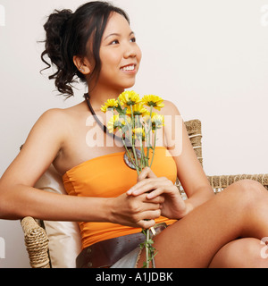 Portrait d'une jeune femme assise sur un fauteuil et holding Flowers Banque D'Images