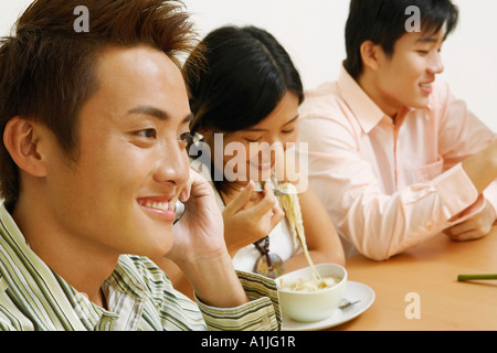 Close-up of a young man talking on a mobile phone avec un jeune couple assis à côté de lui Banque D'Images