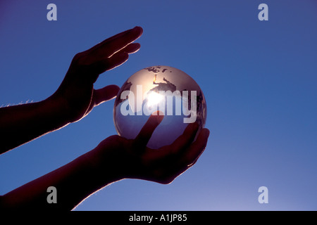 Hands holding Glass globe de cristal de la terre contre un ciel bleu Banque D'Images