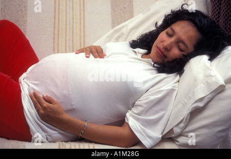 Hispanic Woman en fin de grossesse couchée sur un canapé ayant reste Banque D'Images