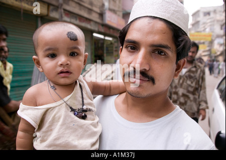 Enfant avec un grand point noir pour conjurer le mauvais œil est tenu par son père dans la région de Dhaka Bangladesh Banque D'Images