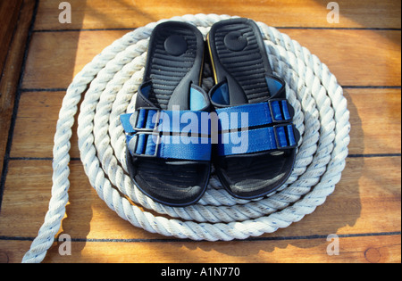 Paire de tongs bleu parfaitement centrée sur une corde enroulée sur le pont en teck d'un voilier Banque D'Images