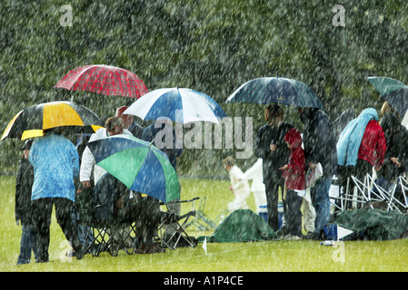 Un groupe de spectateurs à un match de cricket s'exécuter sous couvert d'Umbrella de la pluie. Banque D'Images