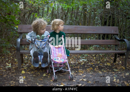 Deux jeunes filles assis sur un banc en bois avec leurs voiturettes de dolly. Banque D'Images