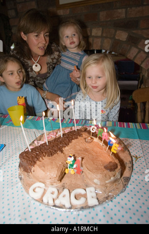 Quatre ans girl blowing out candles on cake au chocolat UK Banque D'Images