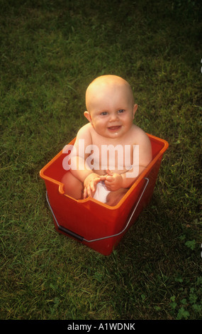 Petit Bébé garçon dans un godet en plastique rouge , à l'extérieur sur un jardin pelouse. Banque D'Images