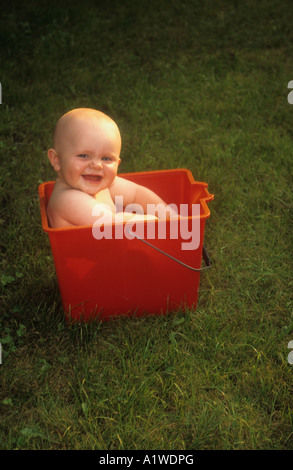 Petit Bébé garçon dans un godet en plastique rouge , à l'extérieur sur un jardin pelouse. Banque D'Images