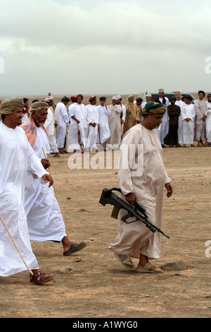 Les hommes avec des épées et des fusils en un cercle, l'un avec une arme d'assaut automatique lors d'une célébration, Salalah, Oman Banque D'Images