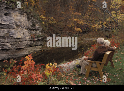 Senior couple bénéficiant d'une soirée d'automne sur un banc par creek et hautes falaises Midwest USA Banque D'Images