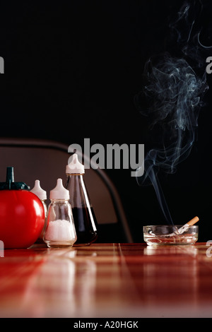 Cigarette dans le cendrier sur la table avec des condiments Banque D'Images