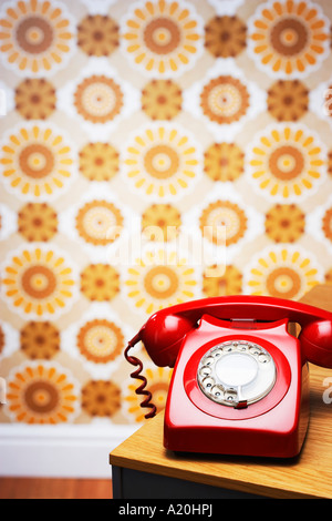 Old fashioned téléphone rouge sur la table en face de papier peint fleuri Banque D'Images