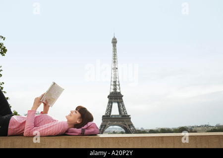 France, Paris, young woman reading book sur balcon en face de la Tour Eiffel Banque D'Images