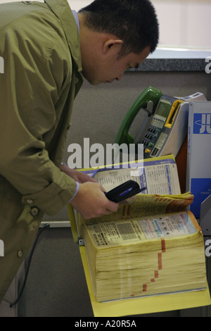L'homme japonais à l'aide de l'annuaire et du téléphone mobile. Tokyo, Japon Banque D'Images