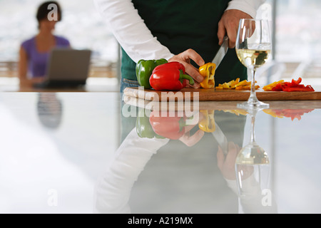 Man (mid section) Couper les poivrons en face de femme sur lap top dans la cuisine, l'accent sur le premier plan Banque D'Images