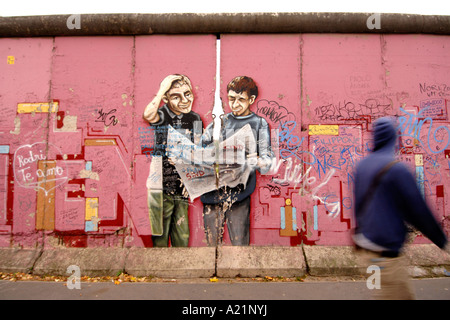 Un homme passe devant une peinture murale rose colorée à l'East Side Gallery, une partie de l'ancien mur de Berlin à Berlin Est. Banque D'Images