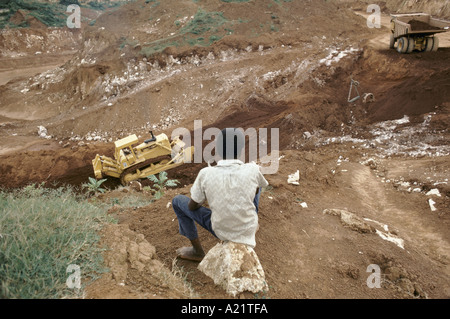 Un enfant assis à une mine de bauxite avec véhicules de construction sur site, Jamaïque, Caraïbes Banque D'Images