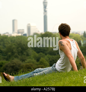 Jeune homme s'assied sur Primrose Hill avec la ville de Londres en arrière-plan dans l'été Banque D'Images