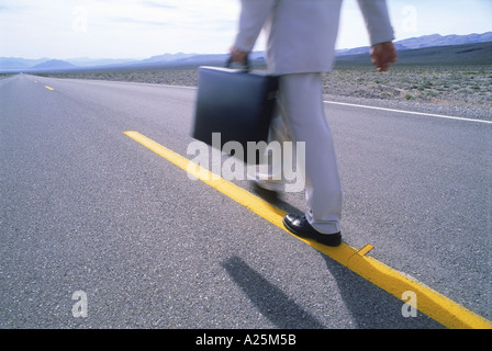 Businessman with briefcase walking long lonely highway Banque D'Images