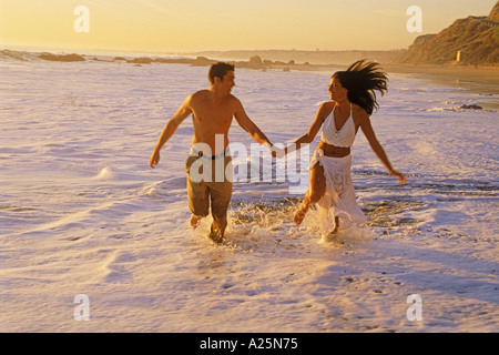 Couple heureux moments romantiques dans des vagues se brisant sur la côte de sable le long de la côte sud de la Californie au coucher du soleil Banque D'Images