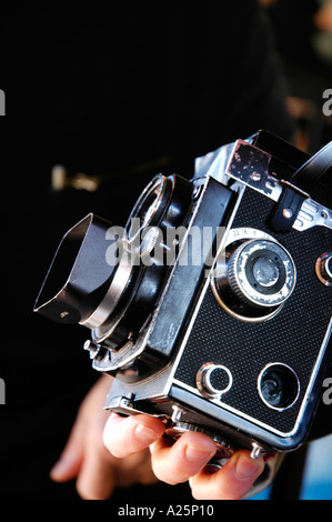 Ancien appareil photo reflex bi-objectif Yashica étant tenue à la main sur un fond noir Banque D'Images