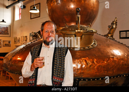 Un homme bénéficie d'un verre de whiskey derrière un vieux pot (encore un géant électrique en cuivre) utilisé pour la distillation dans le bushmills Banque D'Images