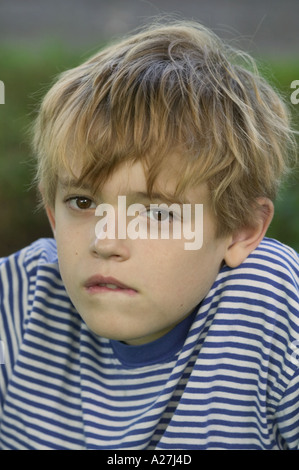 Huit ans garçon blond en chemise rayée biting lip Banque D'Images