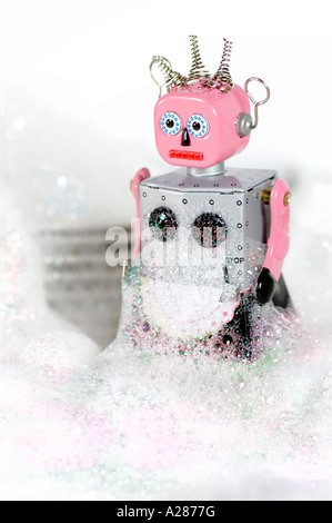 Femme tin toy robot debout devant des plats et couverts dans de l'eau savonneuse ou le liquide vaisselle bubbles Banque D'Images