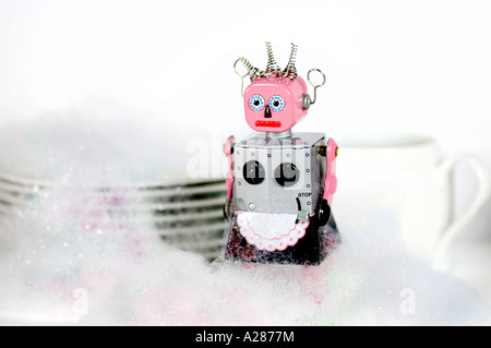 Femme tin toy robot debout devant des plats et couverts dans de l'eau savonneuse ou le liquide vaisselle bubbles Banque D'Images