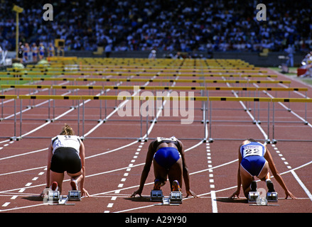 Vu de derrière trois coureuses féminines sur leurs blocs de départ à la recherche en bas de la voie avant une course de 100m haies Banque D'Images