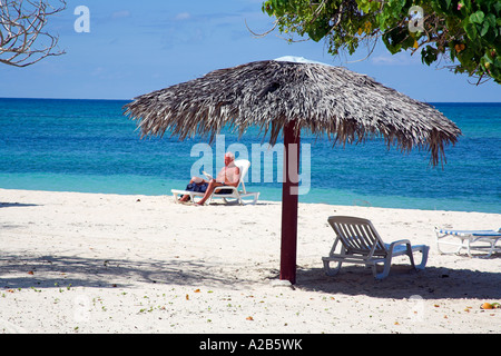 Détente homme près d'un parasol sur une plage, Guardalavaca, Holguin, Cuba Province Banque D'Images