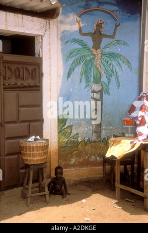 Enfant africain à l'ombre par une peinture murale voodoo, Ouidah, Bénin. Banque D'Images