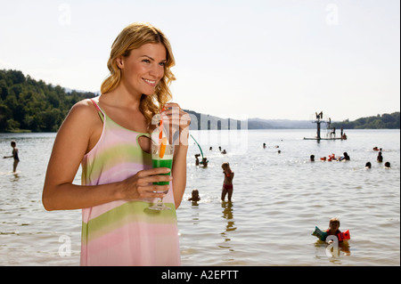 Woman holding cocktail au lac, smiling Banque D'Images