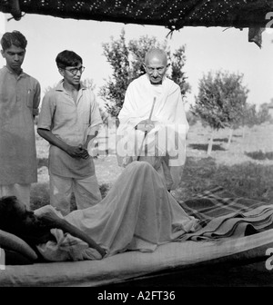 Mahatma Gandhi debout bâton en main avec deux autres personnes parlant à un patient allongé dormir sur le lit à Sevagram Ashram Wardha Nagpur Inde 1941 Banque D'Images