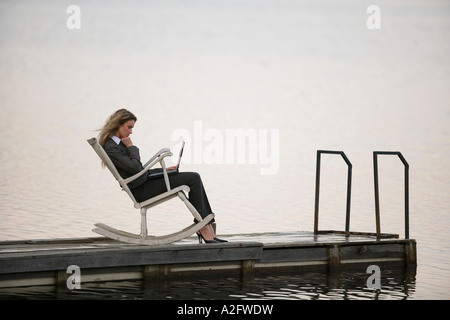 Businesswoman sitting in rocking chair on Jetty, using laptop, side view Banque D'Images