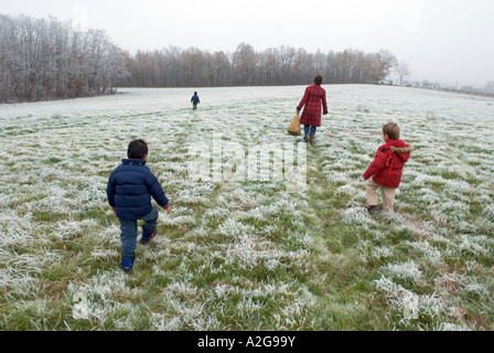 Trois jeunes garçons et leur maman marcher à travers un champ couvert de givre loin de camera Banque D'Images