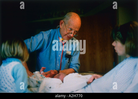 Le pédiatre examine bébé nouveau-né dans la chambre de naissance tandis que sa soeur aînée et sa mère regarder sur Banque D'Images