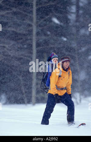 Une mère porte son bébé dans un sac à dos qu'elle porte-raquettes à travers un champ sur un jour de neige Banque D'Images